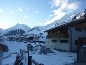 Un pueblo cubierto de nieve con edificios de estilo chalete, un telesilla y un pico montañoso prominente al fondo.