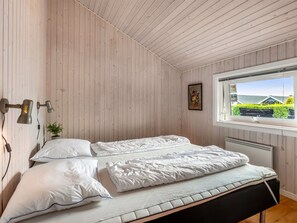 Ein Zimmer mit einem Bett, einem Fenster mit Blick, einer Wandlampe und einer kleinen Pflanze.