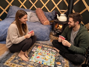 Two people playing a board game on a patterned rug in a room with a bed, a wooden headboard, and a wood-burning stove. - Holt - Glamping Yurt (Holt)