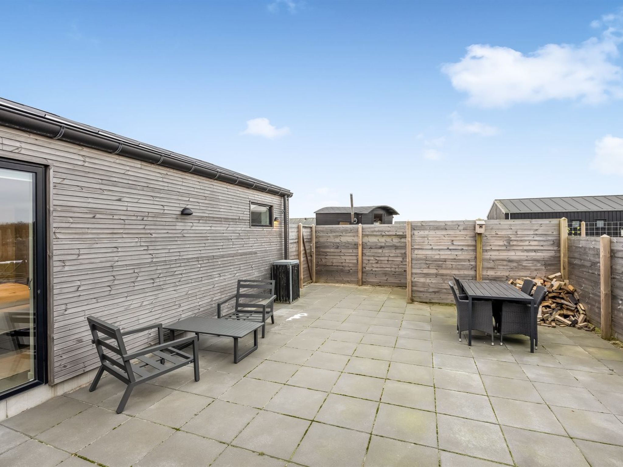 A patio with a table and chairs, a wooden fence, and a building with a window.