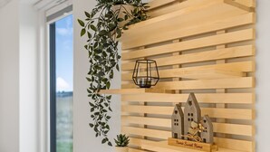 Een muur met horizontale houten latten, een hangplant, een lantaarn en een klein huisvormig decoratie met een bordje.