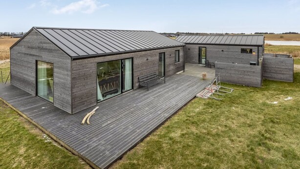 Een modern huis met een groot terras, een overdekte zithoek en uitzicht op het omliggende landschap.