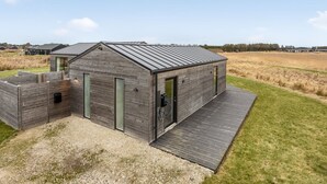 Een modern houten blokhut met een schuin dak, een overdekt buitengedeelte en uitzicht op het platteland.