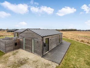 Eine moderne Holz-Blockhütte mit geneigtem Dach, einer überdachten Terrasse und Blick auf eine ländliche Landschaft.