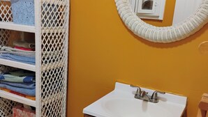 Un baño con un mueble de almacenamiento de mimbre blanco, un lavabo blanco y un armario de madera.
