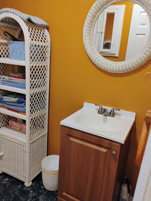 Ein Badezimmer mit einem weißen Korbschrank, einem weißen Waschbecken und einem Holzkabinet.