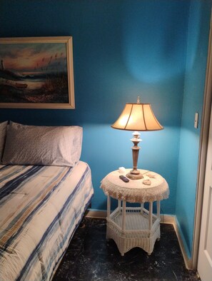 Ein Schlafzimmer mit einem Bett, einem Nachttisch mit Lampe, einem Bild an der Wand und einer blauen Wand.