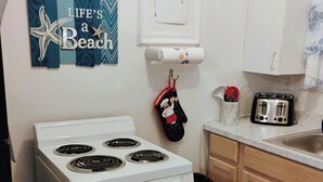 Una cocina compacta con estufa blanca, armarios de madera y encimera de mármol, además de un pequeño cubo de basura.