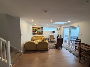 Ein Wohnzimmer mit einer Couch, einem Sessel, einem Gemälde und einer Schiebetür zu einem Außenbereich.