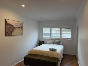 A bedroom with a bed, a bench, a picture on the wall, and a window with blinds.