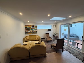 Una sala de estar con un sofá, sillones, un cuadro y un ventanal corredera a un patio.