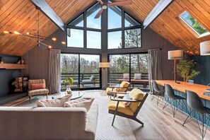 Ein geräumiger Raum mit hoher Decke, großen Fenstern, Holzboden und einer Essecke mit Stühlen und einem Tisch.