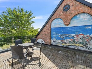 Eine Dachterrasse mit Wandgemälde, Gartenmöbeln und Blick auf Bäume.