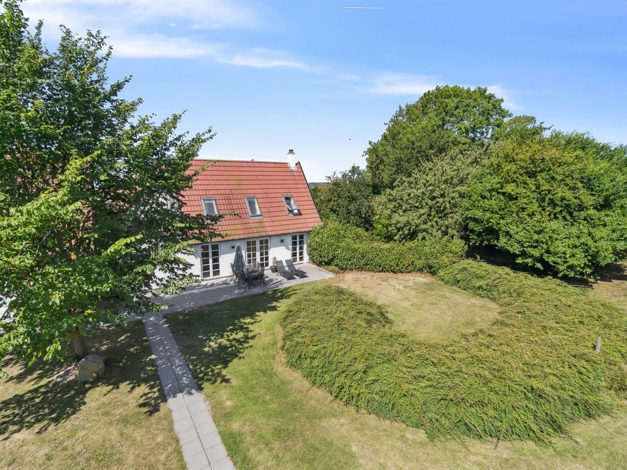 A house with a red roof, surrounded by greenery and a paved driveway.