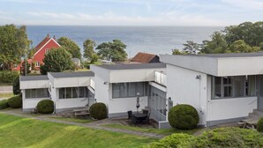 Une maison moderne à deux étages, dotée d’un balcon, d’une terrasse avec mobilier d’extérieur et offrant une vue sur la mer.