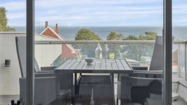 Un balcon avec des meubles en osier, une table et une bouteille.
