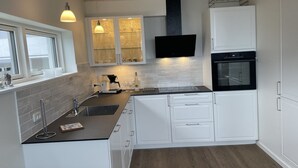 Une cuisine moderne avec des meubles blancs, un plan de travail noir, un four encastré et des luminaires suspendus.
