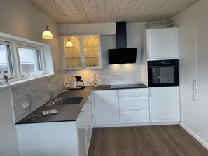 Een moderne keuken met witte kasten, een zwart aanrecht, een inbouwoven en hanglampen.