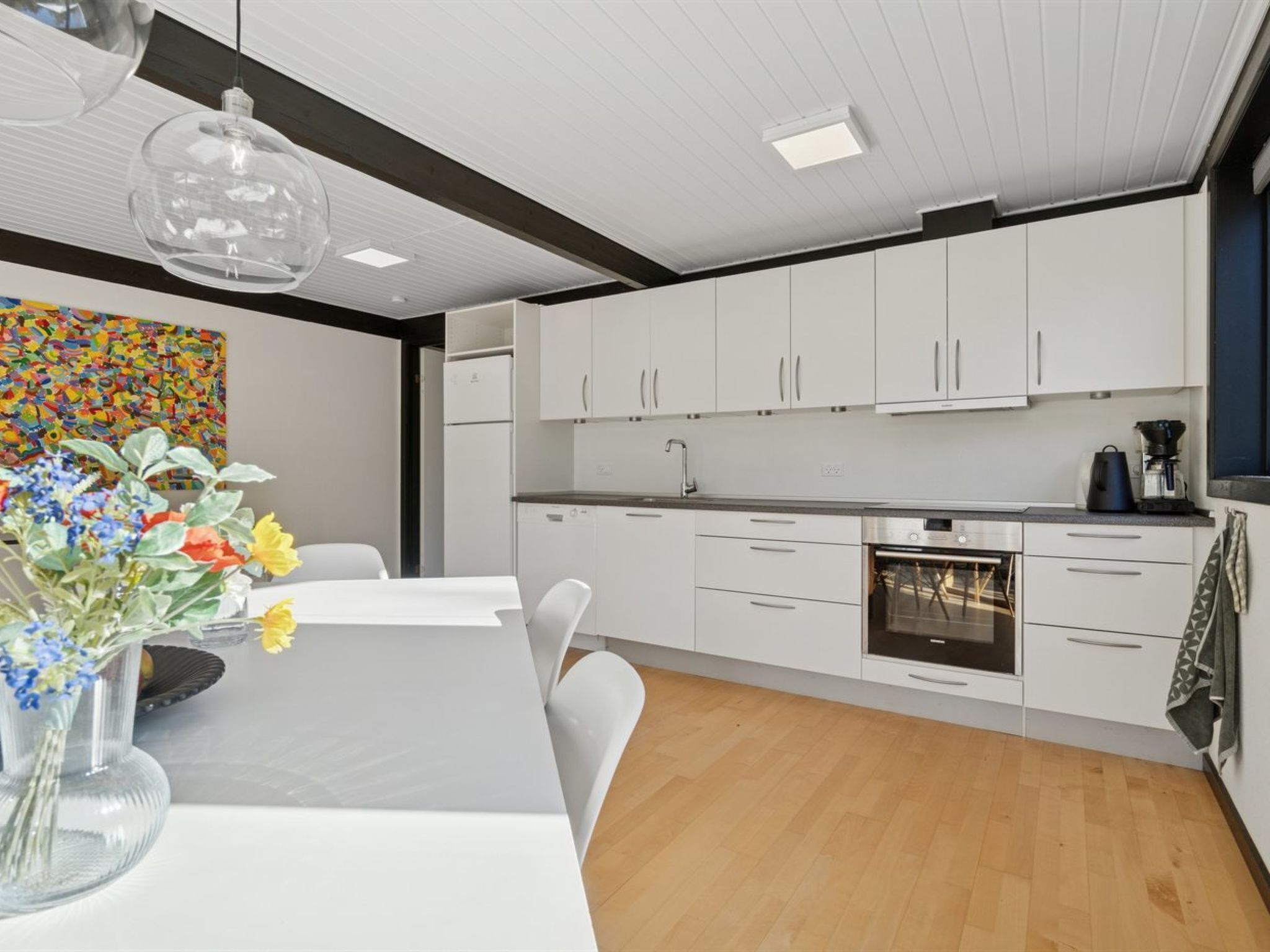Una cocina moderna con armarios blancos, un horno de acero inoxidable y un comedor con mesa y sillas.