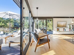 Ein modernes Interieur mit einer großen Glaswand, Holzböden und einer Sitzecke mit Blick ins Freie.