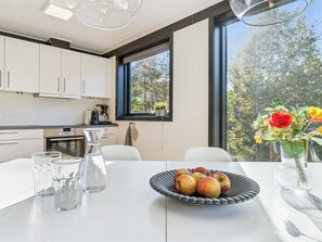 Eine moderne Küche mit weißen Schränken, einer Kaffeemaschine und einem großen Fenster mit Blick auf Bäume.