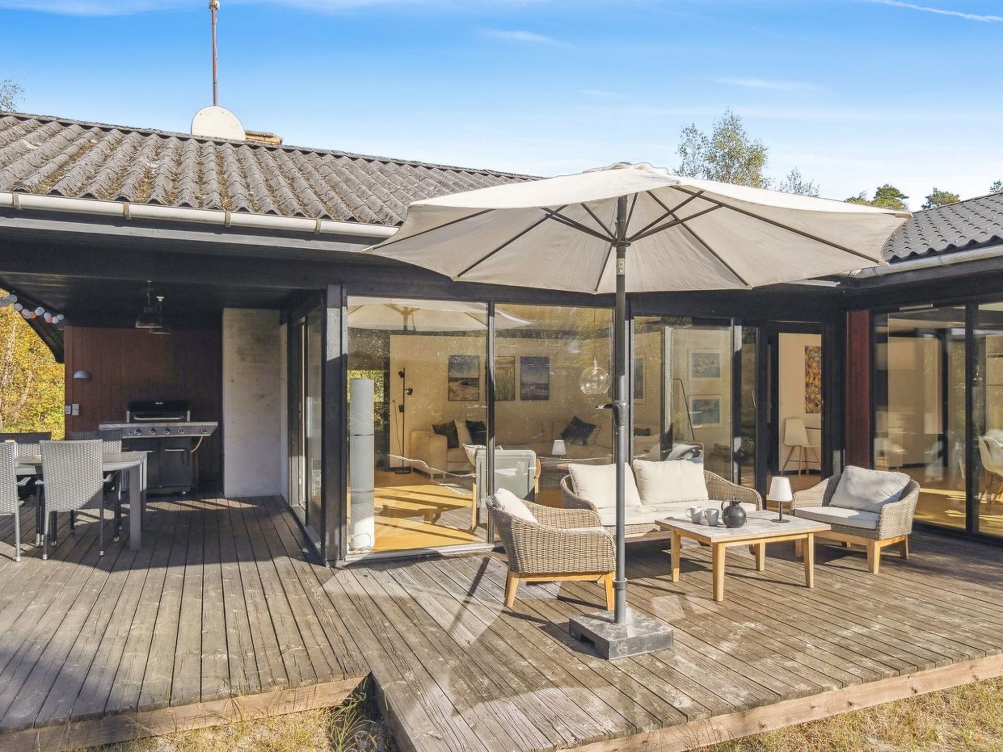 Eine überdachte Terrasse im Freien mit Grill, Sitzgelegenheit und einem großen Sonnenschirm.