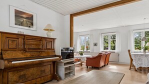 A spacious living room with a wooden piano, a television, and a dining area with a table and chairs. - "Hening" - 150m from the sea by Interhome (Allinge)
