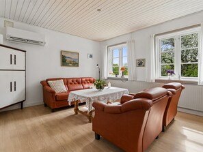 Una habitación con un sofá de cuero marrón, una mesa de comedor con mantel de encaje y un ventanal con vistas a zonas verdes.