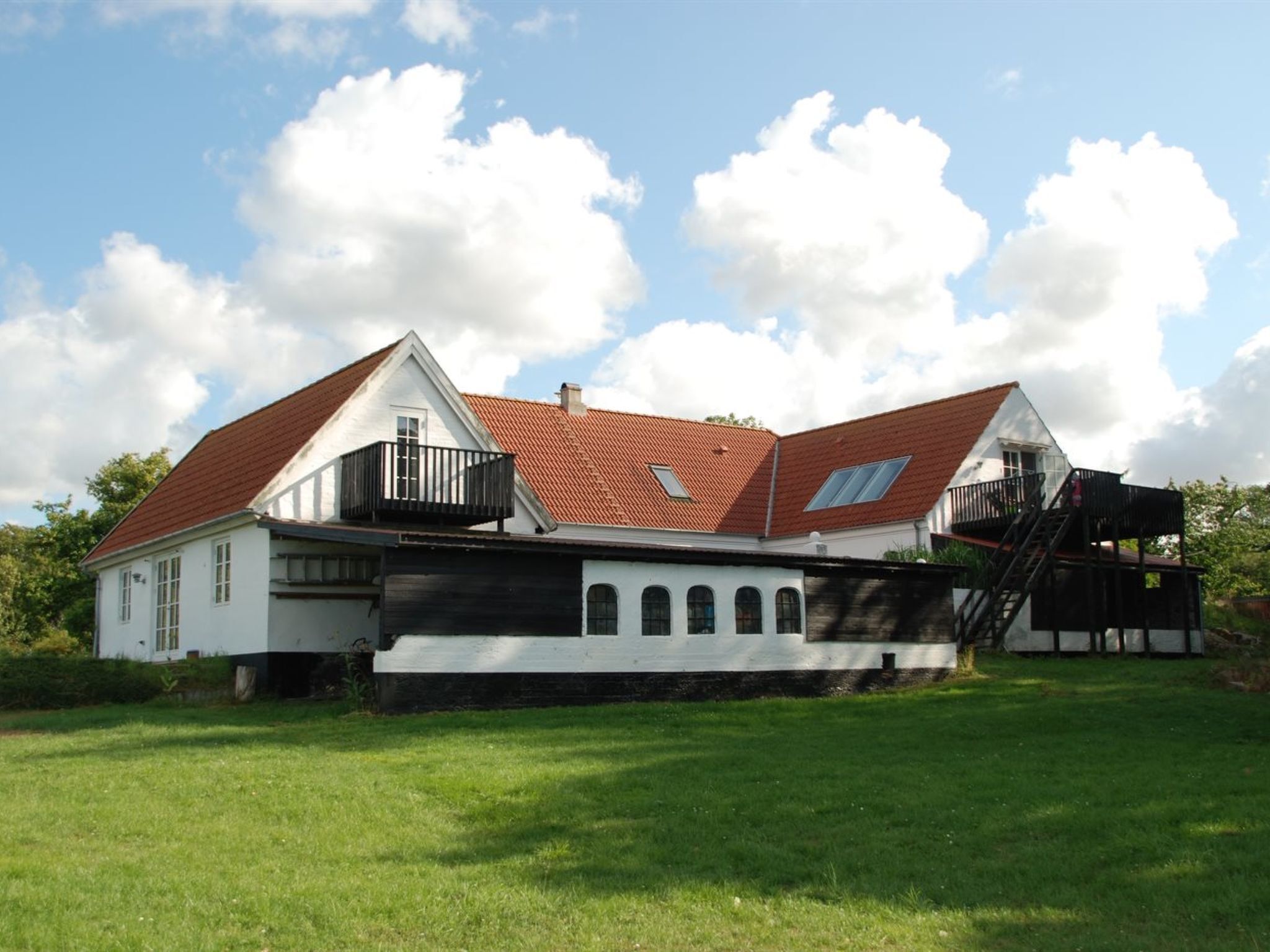 Une maison à deux étages, avec un toit recouvert de tuiles rouges, des murs extérieurs blancs et un balcon à l’étage supérieur.