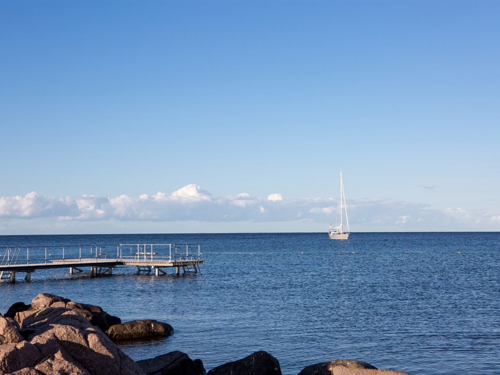 A pier extending into calm waters with a sailboat in the distance.