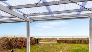 Un patio techado con vistas al mar, un área con césped y una mesa y silla blancas.