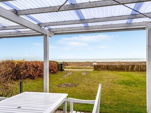 A covered patio with a view of the sea, a grassy area, and a white table and chair. - "Richard" - 400m from the sea by Interhome (Frederikshavn)