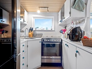 A modern kitchen with white cabinets, a built-in oven, a microwave, and a window above the sink. - "Richard" - 400m from the sea by Interhome (Frederikshavn)