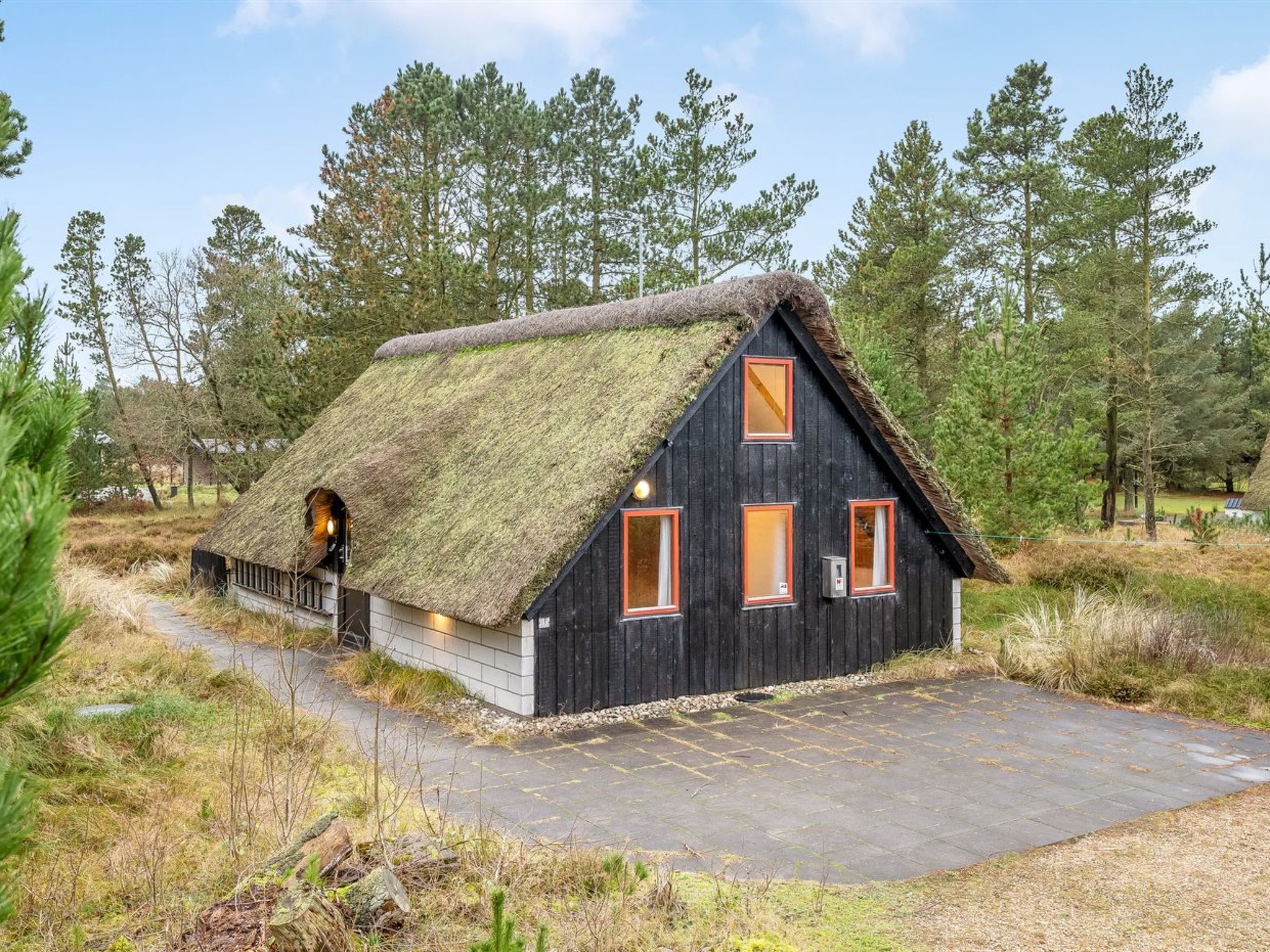 Une cabane au toit de chaume, avec une façade en bois, une allée pavée et un paysage naturel environnant.
