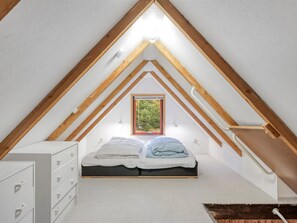 Ein Schlafzimmer mit schrägem Dach, einem Bett, einer Kommode und einem Fenster.