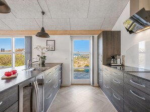 Eine moderne Küche mit einer großen Kochinsel, Edelstahlgeräten und Blick durch eine Schiebetür.