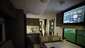 Een compact camperinterieur met een kitchenette, een eethoek en een televisie waarop streamingdiensten worden weergegeven.