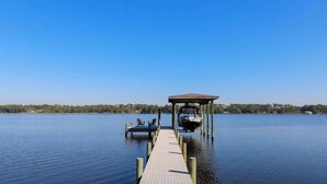 A wooden dock extending into a calm lake with a covered boat house and chairs at the end.