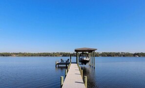 A wooden dock extending into a calm lake with a covered boat house and chairs at the end.