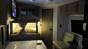 Een compact RV-interieur met een bed, een klein tafeltje, een bank en een aan de muur bevestigde televisie.