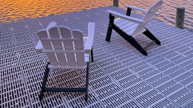 Een houten steiger met twee Adirondack stoelen gericht op een zonsondergang boven een rustig wateroppervlak.