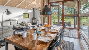 A modern interior with a wooden ceiling, a fireplace, a dining area with a table set for four, and a sofa.