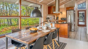 A modern kitchen with a central island, large windows, and a dining area with a wooden table and chairs.