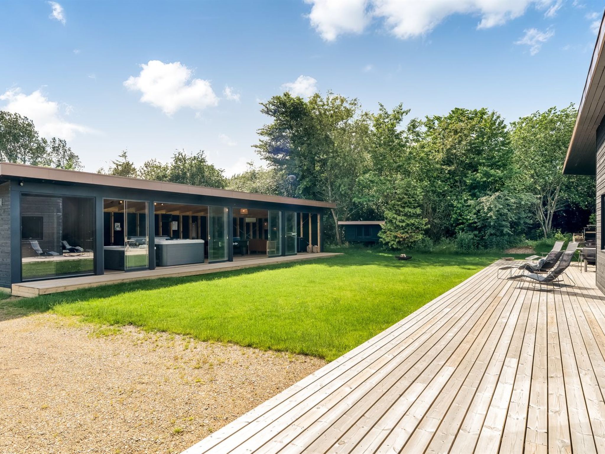 Een modern huis met een grote glazen patio, een houten terras en een verzorgd gazon.