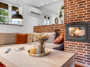 Ein gemütliches Wohnzimmer mit Kamin aus Ziegelsteinen, einer Couch, einem Couchtisch mit Kerzen und einer hängenden Pendelleuchte.