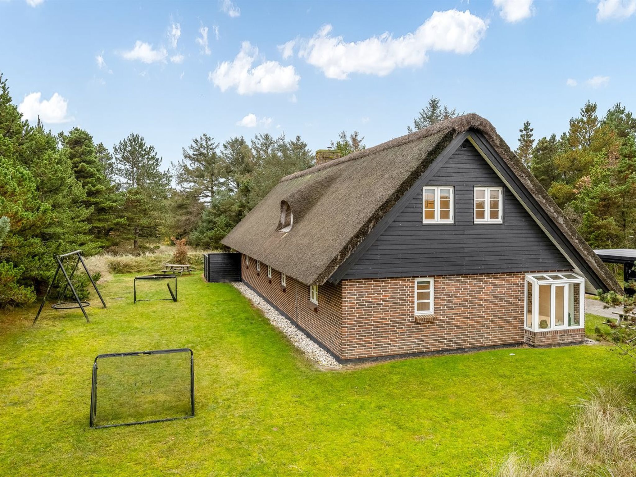 A house with a thatched roof, brick walls, and a small attached shed.
