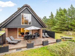 Ein Haus mit geneigtem Dach, einer Terrasse mit Gartenmöbeln und einer Ziegel-Fassade.