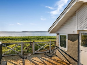 Eine Holzterrasse mit zwei Stühlen, Blick auf das Wasser und ein Gebäude mit weißer Fassade.