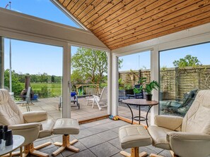 Une véranda dotée de grandes fenêtres, d’un plafond en bois et d’un espace patio aménagé avec du mobilier d’extérieur.