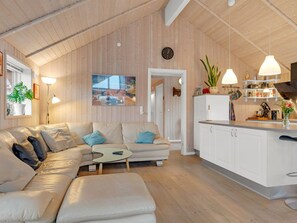 Un interior moderno con un sofá, una mesita, una zona de cocina con armarios y un reloj en la pared.